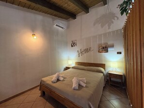 A bedroom with a bed, two bedside tables, a wall-mounted air conditioner, and a wall with a 'Home' sign. - Wonderful  villa for 5 guests with WIFI, A/C, pool, TV, patio and panoramic view (Chiaramonte Gulfi)