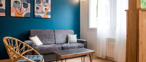 A room with a grey sofa, a wooden coffee table, a wicker chair, and abstract art on the wall.