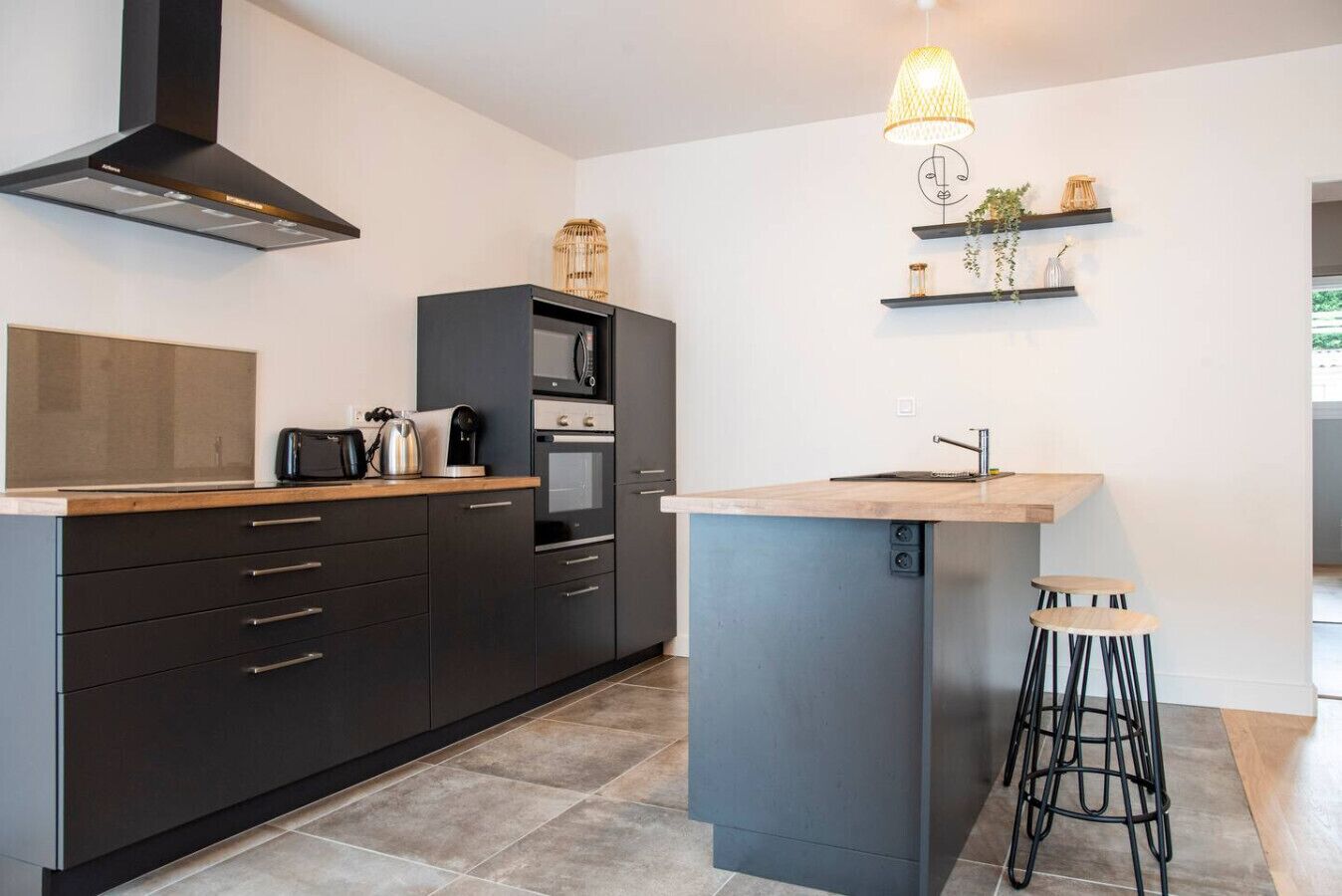 Une cuisine moderne avec des meubles de rangement aux couleurs sombres, un four à micro-ondes encastré et un petit îlot central avec des tabourets.