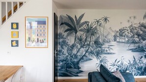 A room with a staircase, a mural of a river scene, and three framed pictures on the wall. - Mansion near downtown and the beach (Granville)