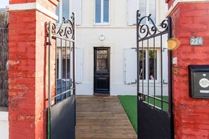A red brick building with a black gate, a wooden pathway, and a black door with a window above it. - Mansion near downtown and the beach (Granville)