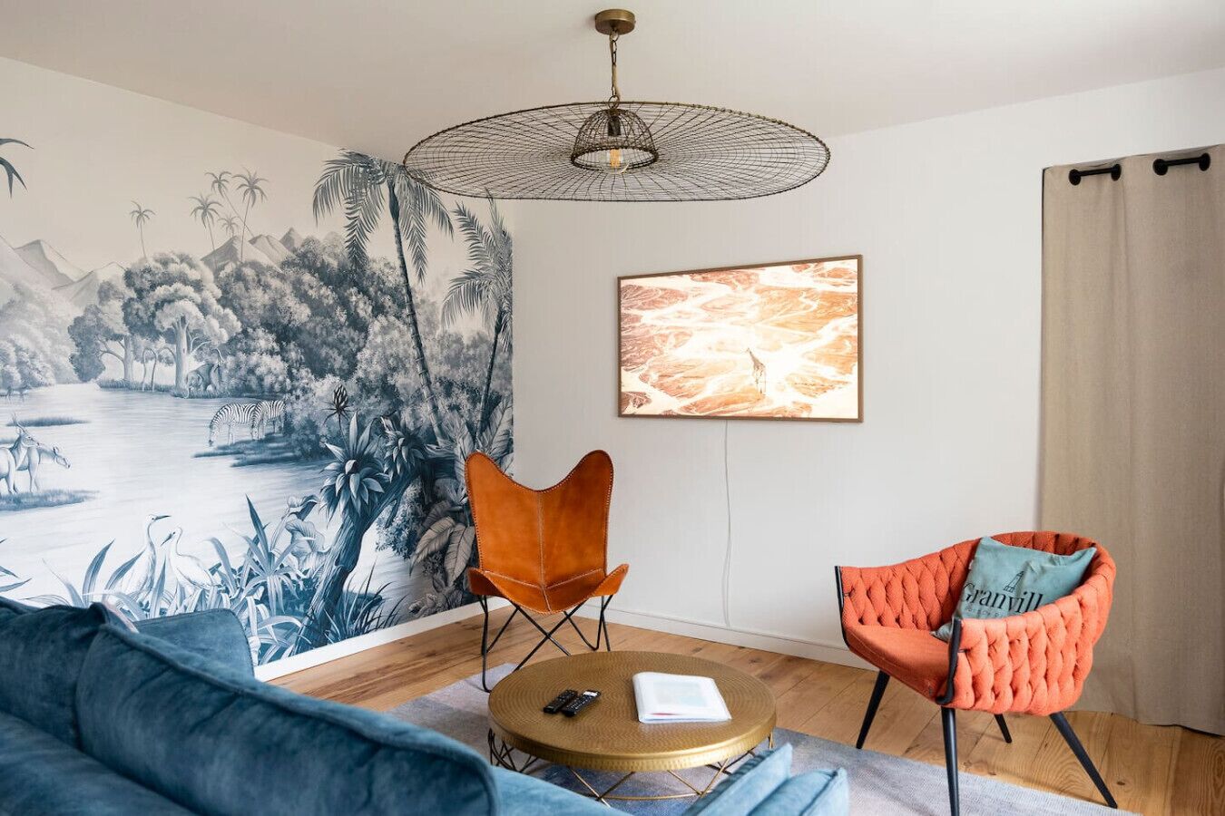 Una habitación con un mural, dos sillas, una mesa redonda y una lámpara en el techo.