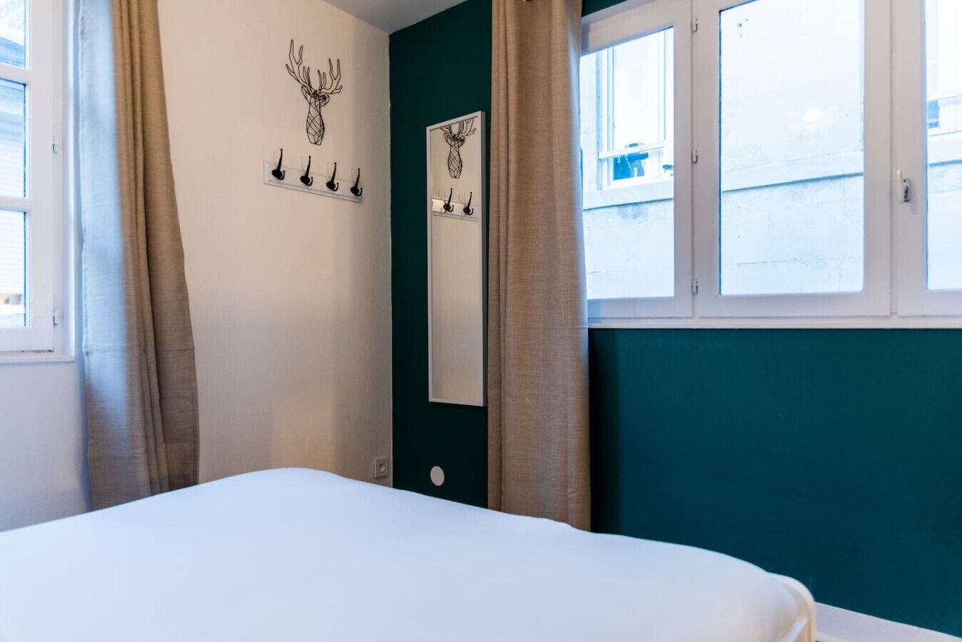 Una habitación con una cama, un espejo montado en la pared y un ventanal con cortinas.