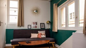 Ett rum med en soffa, ett soffbord, en lampa och ett fönster med gardiner.