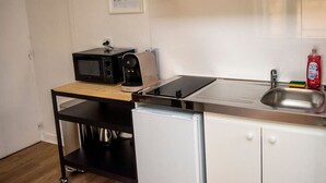 Ett litet, praktiskt kök med en mikrovågsugn, brödrost och kaffebryggare placerade på en rullbar trävagn, en diskho och ett litet kylskåp.