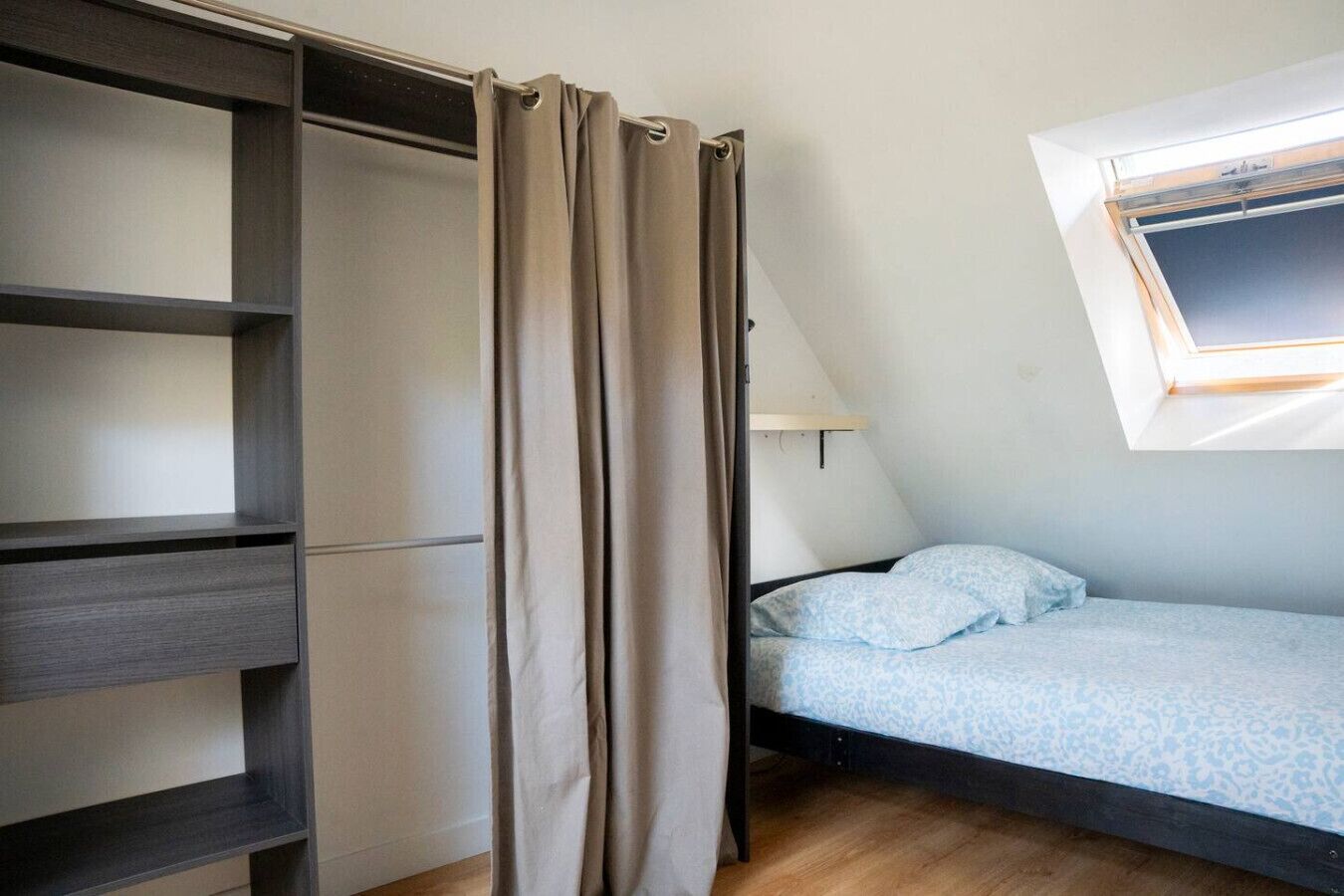 Una camera da letto con un letto, una finestra vista, un mobiletto a scaffali e una tenda.