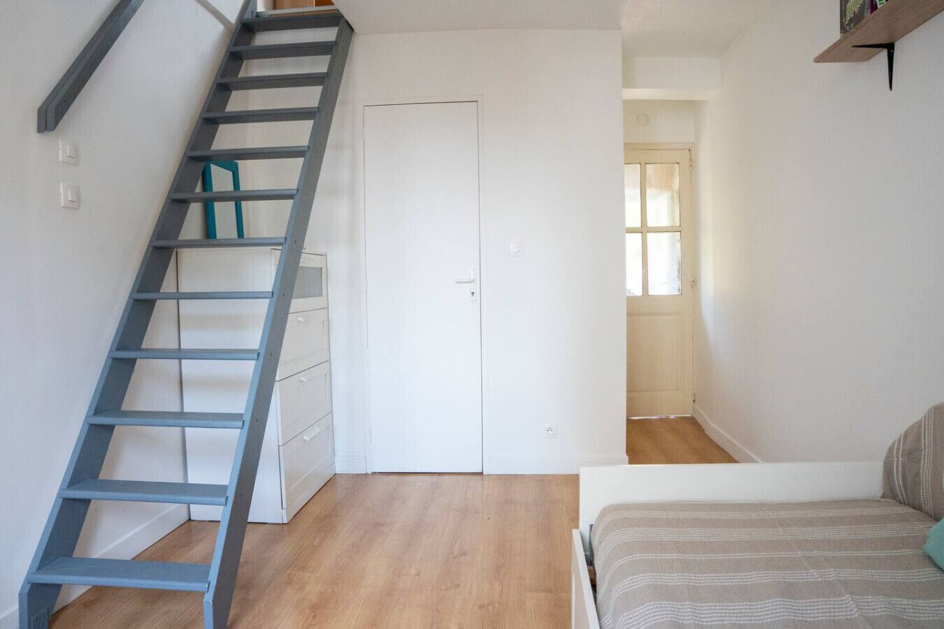 Ein Schlafzimmer mit einem Bett, Holzboden, einer weißen Tür und einer blauen Treppe.