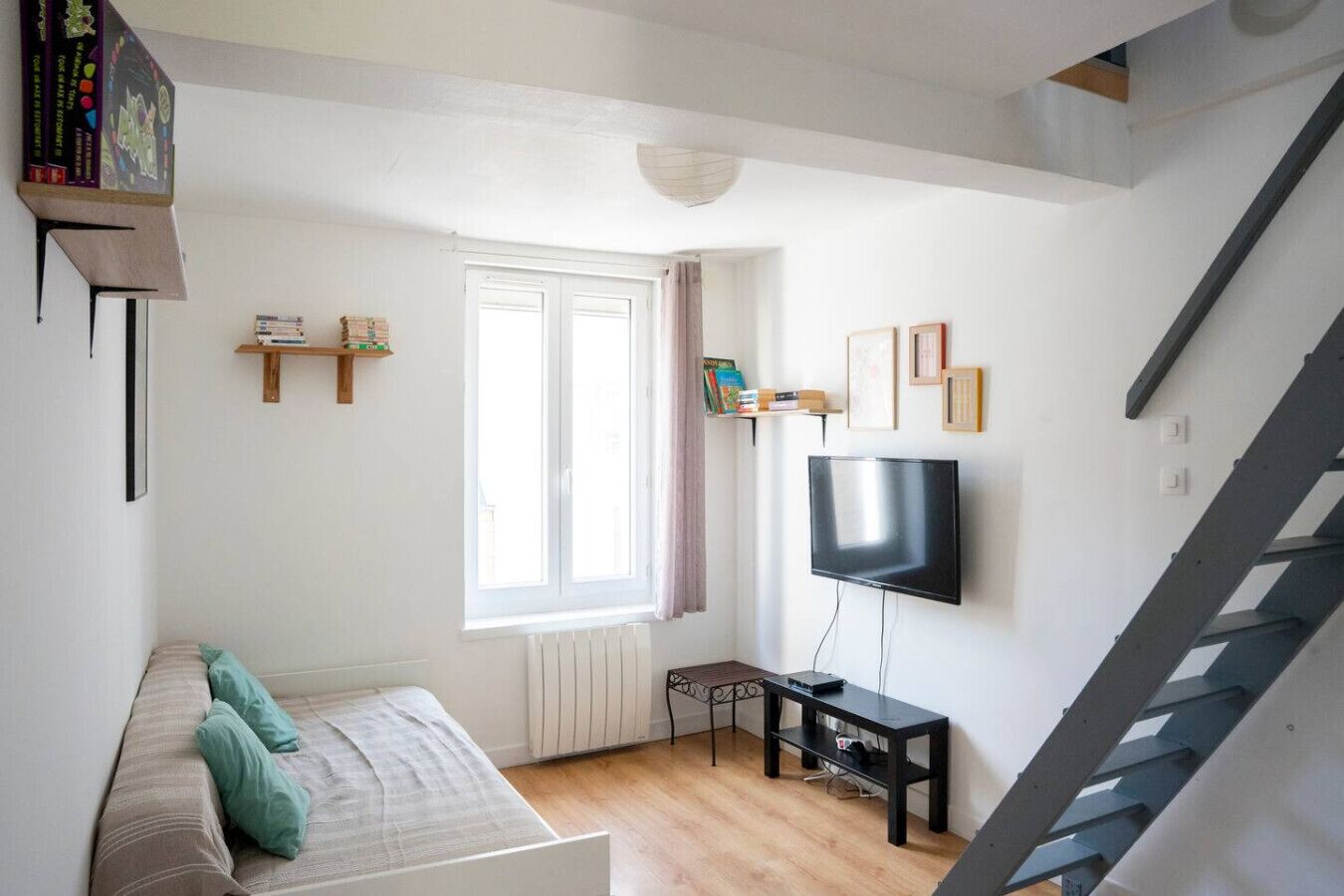 Ein Wohnzimmer mit einer Couch, einem Fernseher, einem Fenster und einer Treppe.