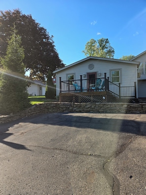 A single-story house with a stone foundation, a front porch with a railing, and a small set of stairs leading to the entrance. - Cozy 2-bedroom apartment in Berlin. Ohio with AC (Millersburg)