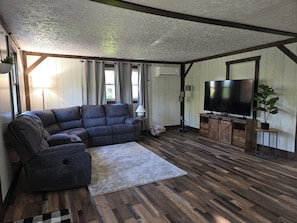 A living room with a sectional sofa, a flat-screen TV, wooden flooring, and a rustic ceiling. - Cozy 2-bedroom apartment in Berlin. Ohio with AC (Millersburg)