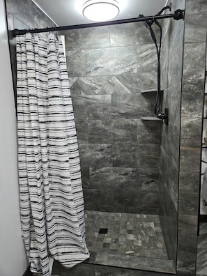 A shower with a black and white striped shower curtain, a handheld showerhead, and a wall-mounted faucet. - Cozy 2-bedroom apartment in Berlin. Ohio with AC (Millersburg)