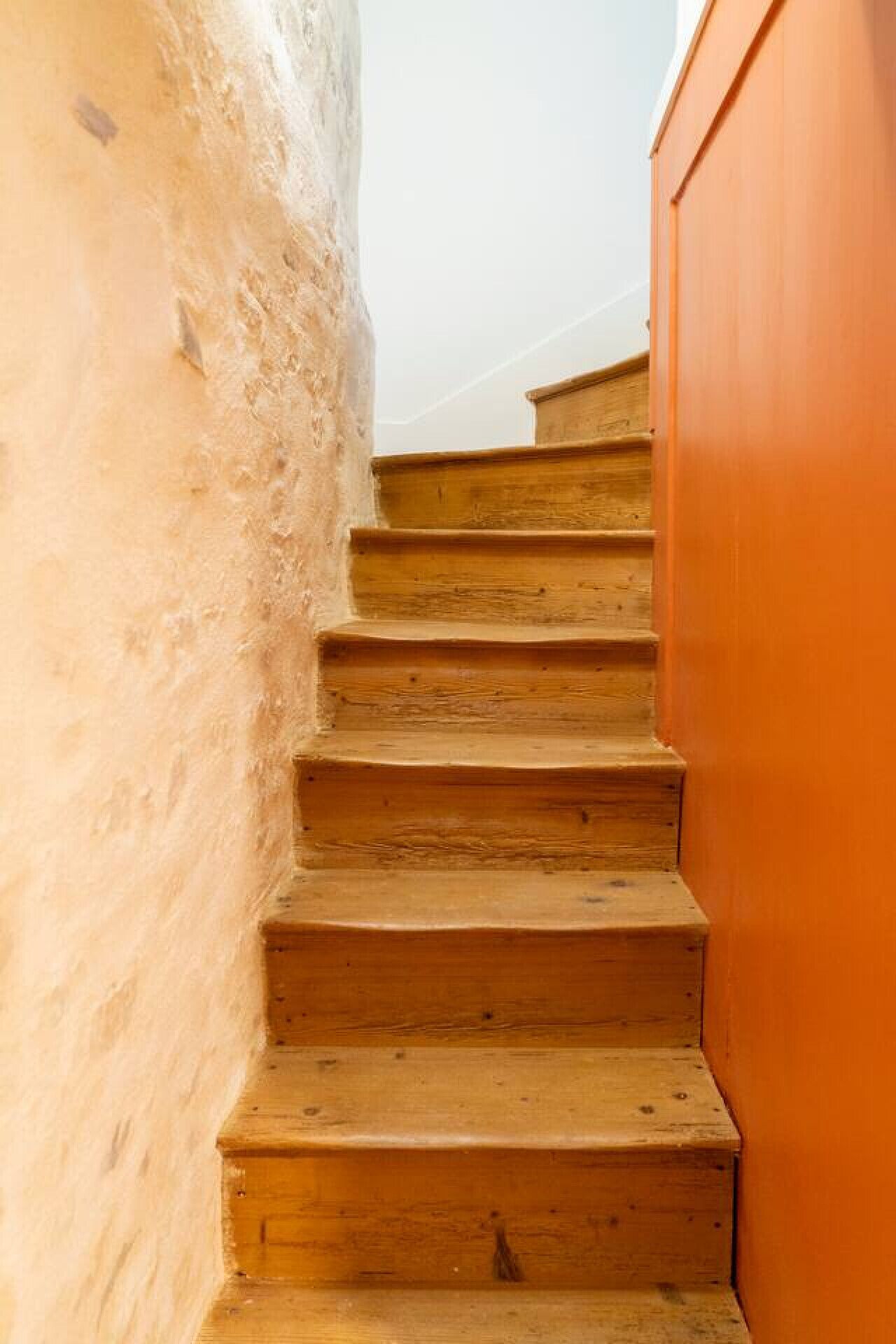 Un escalier en bois, avec un mur rugueux d’un côté et un mur lisse de l’autre.