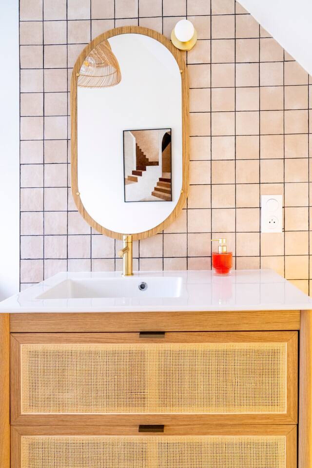 Ein Badezimmer mit Waschbecken, Holzschrank, einem Spiegel mit Bilderrahmen und einem roten Seifenspender.