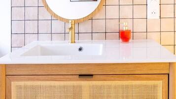 Ein Badezimmer mit Waschbecken, Holzschrank, einem Spiegel mit Bilderrahmen und einem roten Seifenspender.