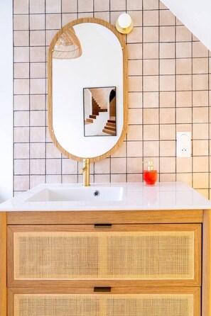 A bathroom with a white sink, wooden vanity, a mirror with a picture frame, and a red soap dispenser.