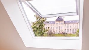 Un dormitorio con tragaluces, una cama con almohadas blancas y naranjas, y vista a un edificio.