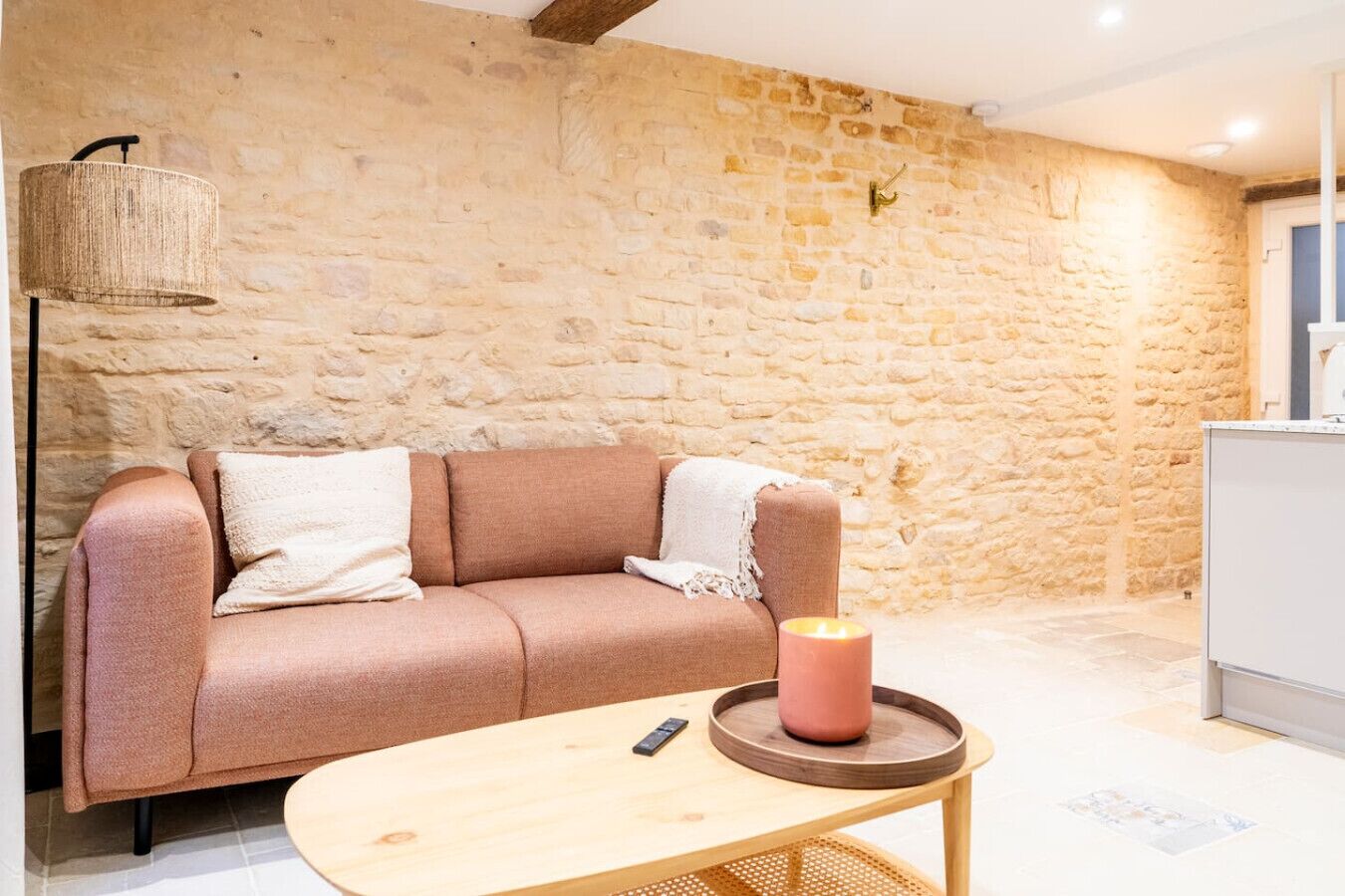 Una habitación acogedora con pared de piedra, un sofá con cojines, una mesita redonda con una vela y una lámpara.