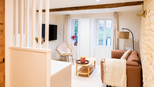 Una habitación con una escalera de madera, una silla de mimbre, un sofá marrón, una mesita con una vela y una lámpara.