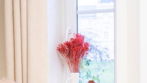 Una silla de mimbre con un cojín mullido, un florero con flores rojas y un objeto con forma de oso en un alféizar.