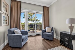 Uma sala de estar com dois poltronas azuis, um aparador preto e uma porta de vidro que dá para um pátio externo.