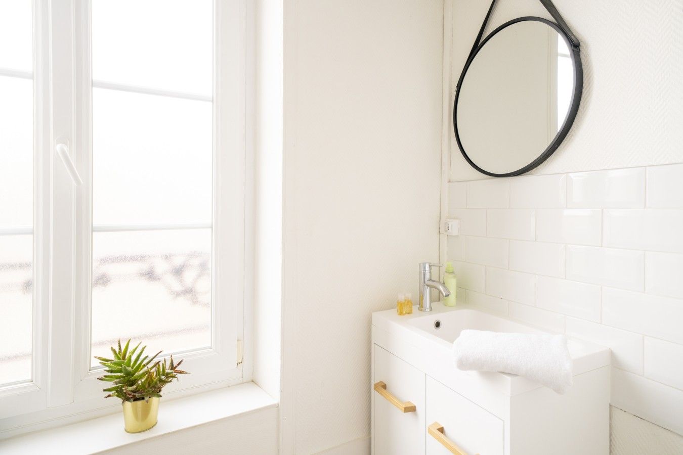 Een badkamer met een wit wastafel, een spiegel en een raam met een plant op de vensterbank.