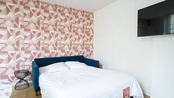 Een slaapkamer met een bed, een aan de muur bevestigde televisie, behang met een patroon en een klein nachtkastje.