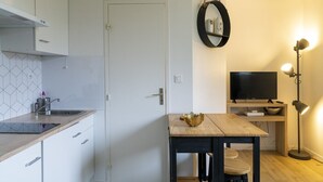 A compact kitchen with a sink, cabinets, a dining table with chairs, a TV, and a floor lamp. - Nice studio apartment for two, near the university (Caen)