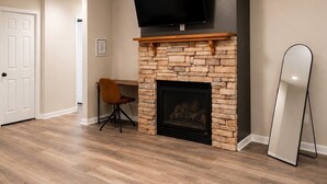 A room with a fireplace, a TV mounted above it, a chair, and a standing mirror.