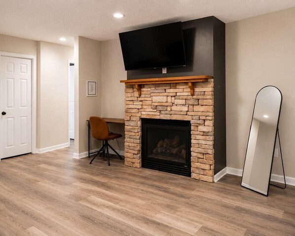A room with a fireplace, a TV mounted above it, a chair, and a standing mirror.