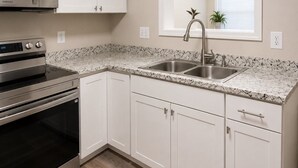 A kitchen with white cabinets, a stainless steel microwave, an oven, a granite countertop, and a sink.
