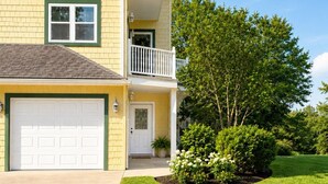 A two-story residential building with a garage, a balcony, and a well-maintained lawn.