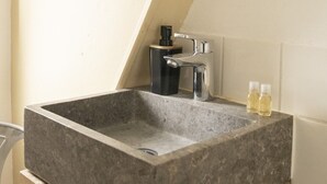 Ett badrum med ett rektangulärt handfat i granit, en spegel, en blandare och en tvålpump.