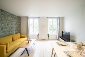 Una sala de estar moderna con un sofá, una mesa de centro, una mesa de comedor para dos personas y un televisor.