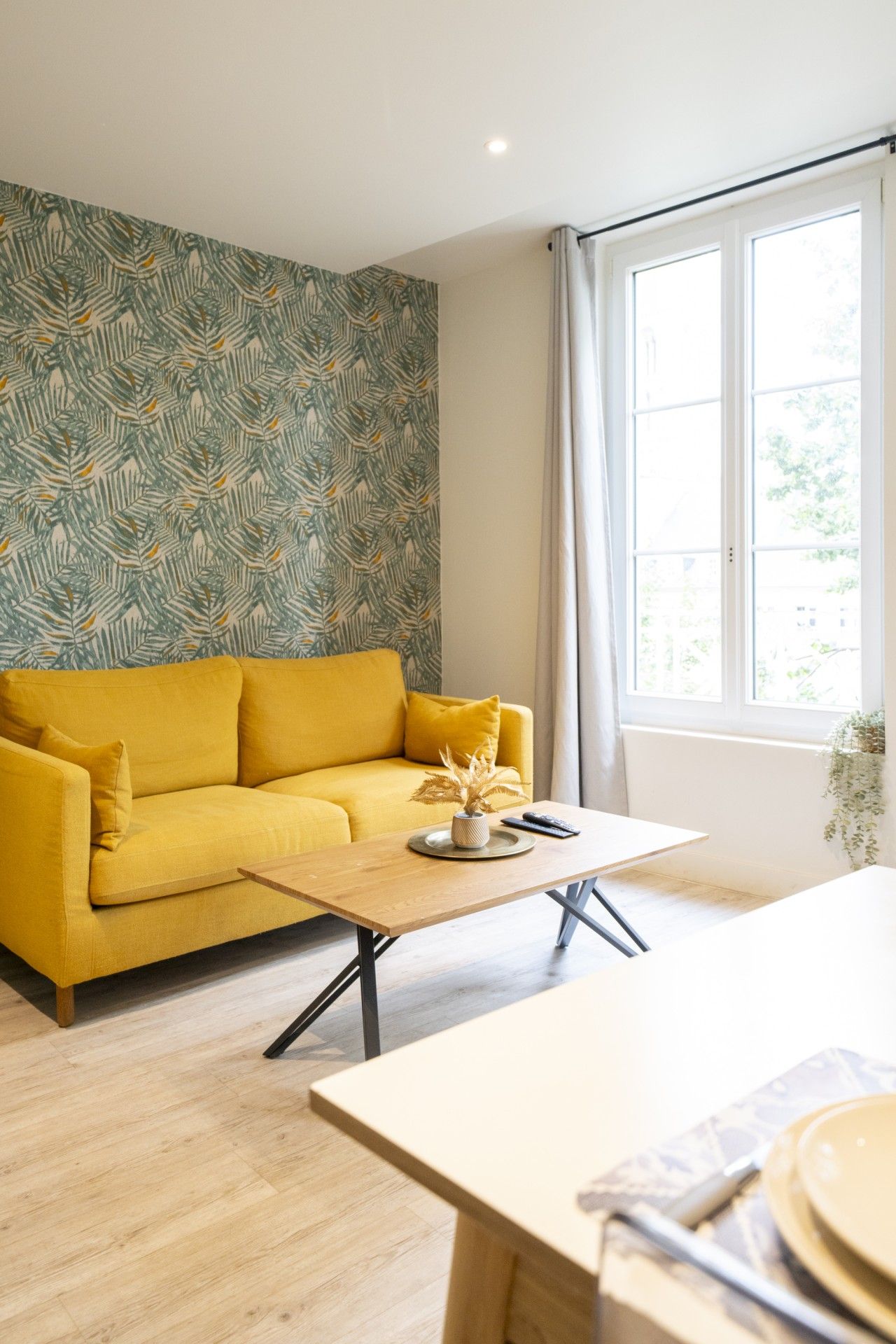 Une pièce avec un canapé jaune, une table basse en bois et une fenêtre avec des rideaux.