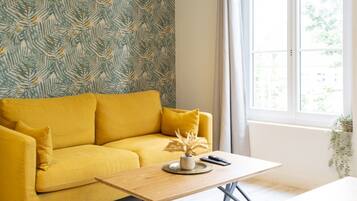 Une pièce avec un canapé jaune, une table basse en bois et une fenêtre avec des rideaux.