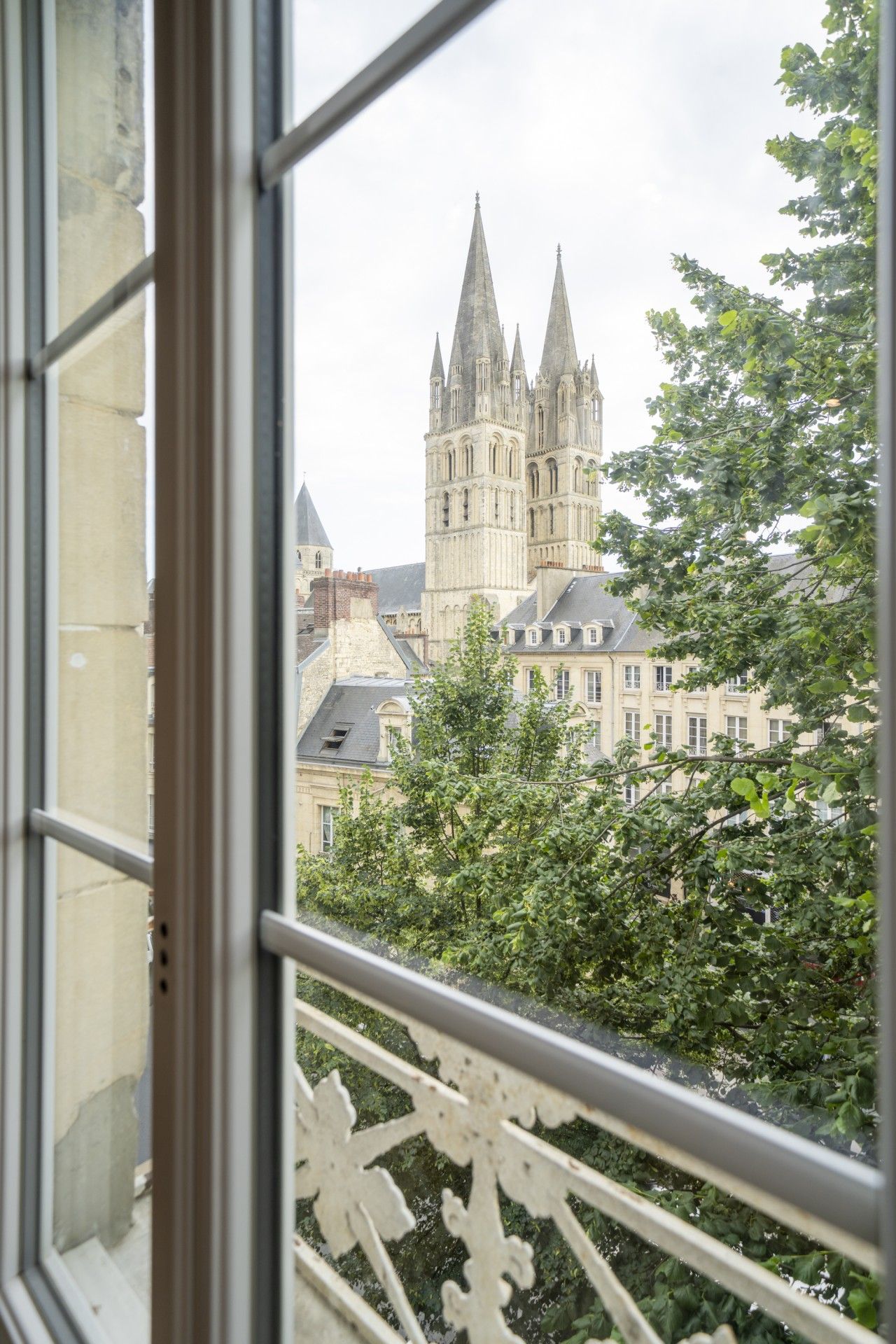 A view through a window with a metal railing, overlooking a historic building with multiple spires and a large, ornate structure.
