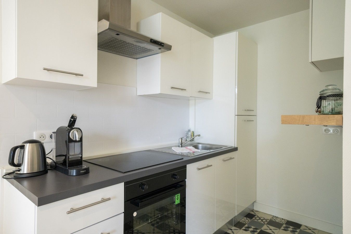 Eine kompakte Küche mit Kaffeemaschine, Wasserkocher, Geschirrspüler und kleinem Backofen.