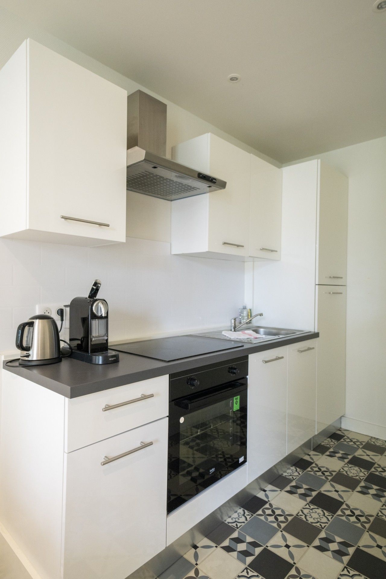 A modern kitchen with white cabinets, a black countertop, a built-in oven, and a patterned tile floor.
