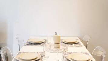 A dining table set for six with clear glassware and plates, a centerpiece, and a framed artwork on the wall.