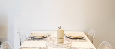Mesa de comedor lista para seis personas, con vasos y platos transparentes, un centro de mesa y una obra de arte enmarcada en la pared.