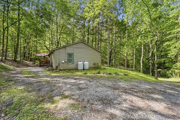 Une petite cabane avec une allée de gravier, entourée d’une forêt dense.