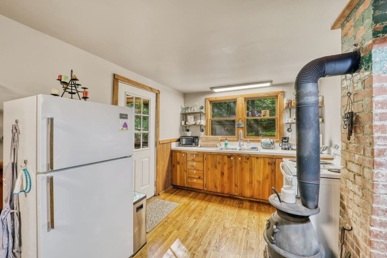 A compact kitchen with wooden cabinets, a white refrigerator, a stove, and a black exhaust pipe.