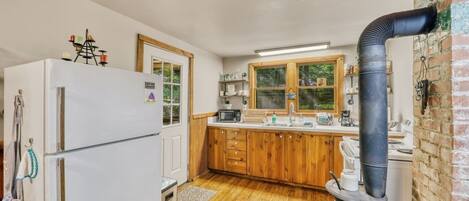 A compact kitchen with wooden cabinets, a white refrigerator, a stove, and a black exhaust pipe.