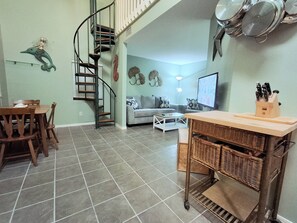 Eine Küche mit Essbereich, einer Wendeltreppe und einem Wohnzimmer inklusive Sofa und Fernseher.
