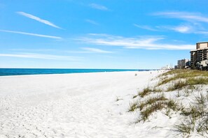 Ein Strand mit weißem Sand, blauem Himmel und Gebäuden im Hintergrund.
