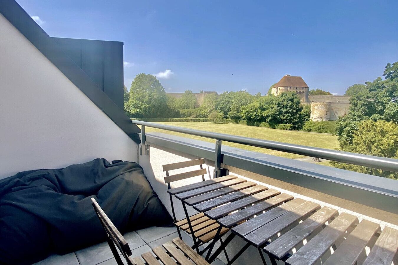 Un balcon donnant sur un château, un banc en bois et un sac noir.