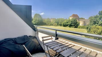 Un balcon donnant sur un château, un banc en bois et un sac noir.