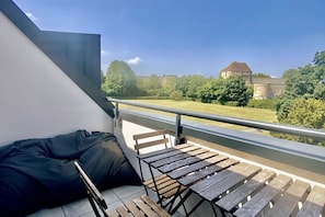 Ein Balkon mit Blick auf ein Schloss, einer hölzernen Bank und einer schwarzen Tasche.