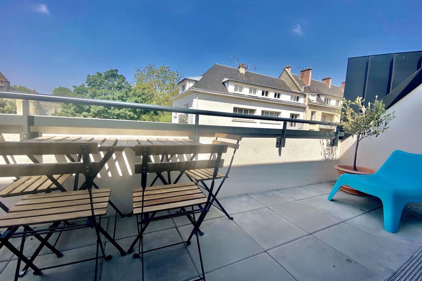 Une terrasse avec une table et des chaises en bois, une chaise en plastique bleue et une plante en pot.