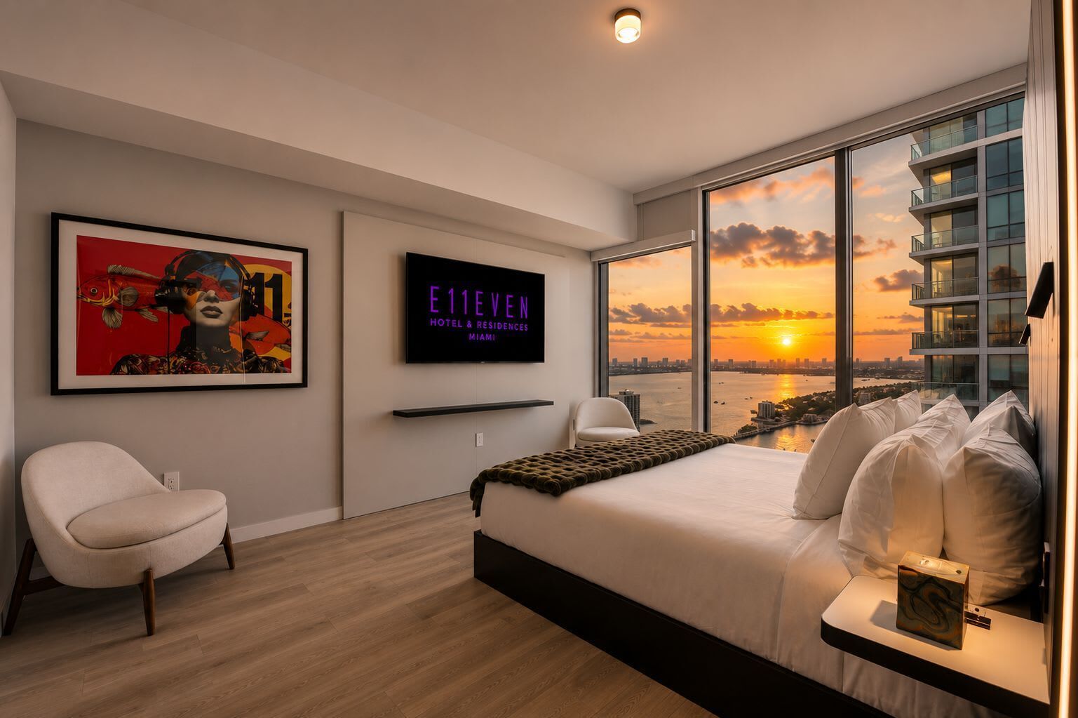 Ein modernes Hotelzimmer mit einem großen Bett, einem Fernseher, einem gerahmten Kunstwerk und Blick auf die Stadt.